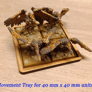 Puede incluir: Una bandeja de movimiento de madera para unidades de 40 mm x 40 mm. La bandeja tiene cuatro compartimentos y est&aacute; pintada de color marr&oacute;n claro. Hay cuatro figuras en miniatura en la bandeja, cada una con alas y una apariencia esquel&eacute;tica.