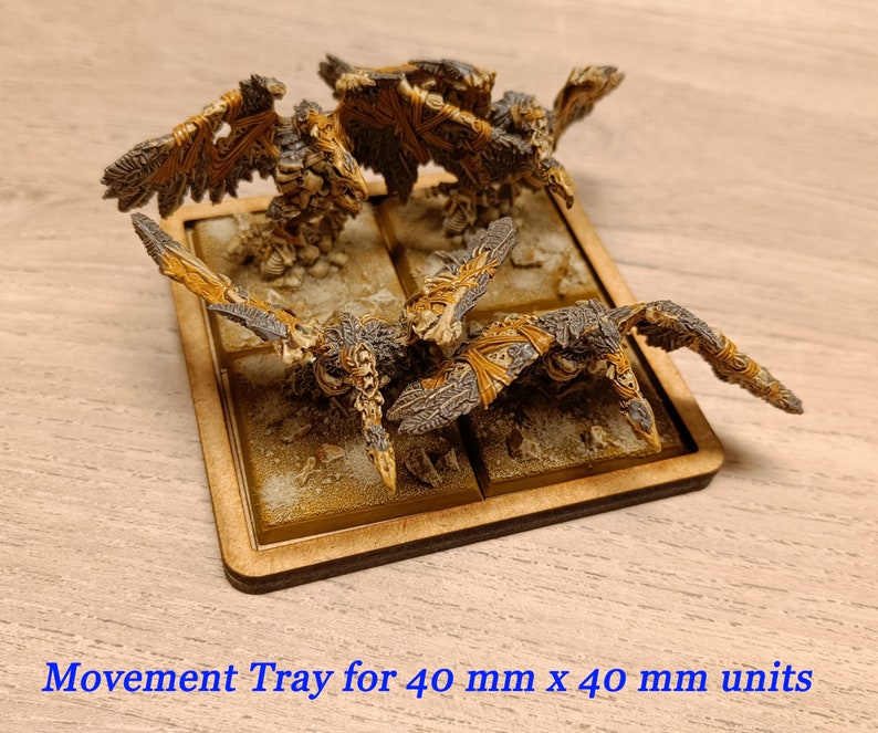 Puede incluir: Una bandeja de movimiento de madera para unidades de 40 mm x 40 mm. La bandeja tiene cuatro compartimentos y est&aacute; pintada de color marr&oacute;n claro. Hay cuatro figuras en miniatura en la bandeja, cada una con alas y una apariencia esquel&eacute;tica.