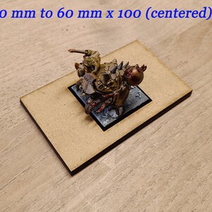 May include: A miniature figure of a green and brown creature with a red eye, mounted on a black square base. The figure is centred on a brown rectangular base, measuring 60 mm by 100 mm.