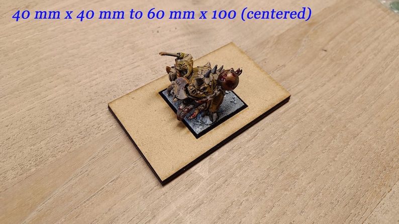May include: A miniature figure of a green and brown creature with a red eye, mounted on a black square base. The figure is centred on a brown rectangular base, measuring 60 mm by 100 mm.