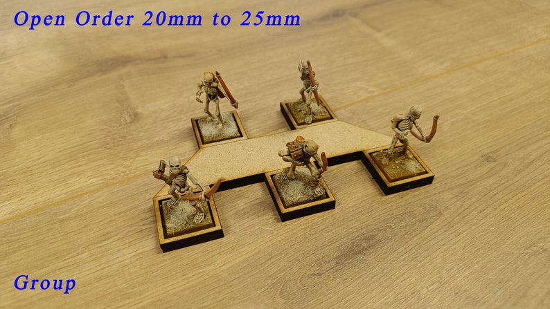 May include: Five miniature skeletal figures with bows and arrows are arranged on a wooden base. The base is shaped like a cross with a central platform. The figures are painted in a light brown colour. The text "Open Order 20mm to 25mm" is visible at the top of the image. The text "Group" is visible at the bottom of the image.
