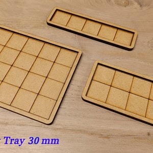 Puede incluir: Tres bandejas de madera con un patr&oacute;n de cuadr&iacute;cula. La bandeja m&aacute;s grande es cuadrada y tiene 25 cuadrados. Las otras dos bandejas son rectangulares y tienen 12 cuadrados cada una. El texto "Movement Tray 30 mm" est&aacute; impreso debajo de las bandejas.