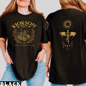 A woman wearing a black t-shirt with a graphic design on the front and a dragon and sun motif on the back.