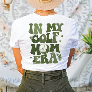 a woman wearing a hat and a tee shirt that says in my golf mom era