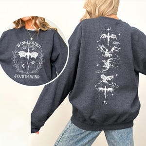 A person wearing a grey sweatshirt with a graphic design featuring a dragon and the text "WINGLEADER FOURTH WING".