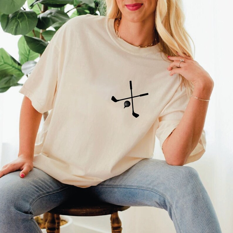 a woman sitting on a stool wearing a t - shirt with a cross on it