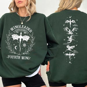 A woman wearing a green sweatshirt with a graphic design featuring a dragon and the text "WINGLEADER" and "FOURTH WING".