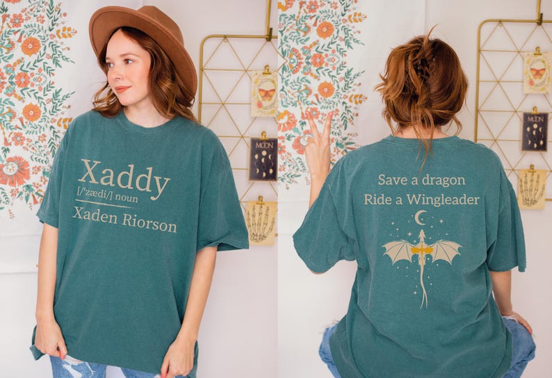 A woman wearing a green t-shirt with a dragon design and text on the back, posing in front of a floral wall.