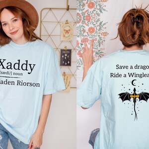 a woman wearing a light blue t-shirt with a dragon design and text on the back.