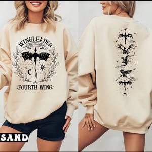 A woman wearing a beige sweatshirt with a graphic design featuring a dragon and the text "WINGLEADER - Fourth Wing" printed on it.