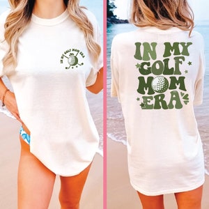 a woman standing on a beach wearing a shirt that says in my golf mom era