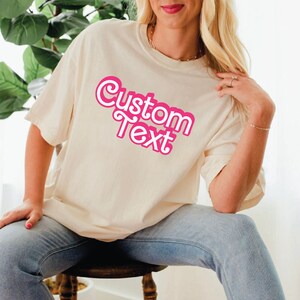 a woman sitting on a stool wearing a t - shirt that says custom text