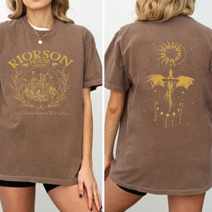 a woman wearing a brown t-shirt with a graphic design on the front and back.