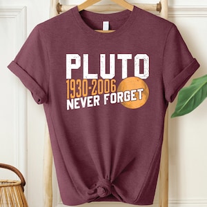 May include: A maroon t-shirt with a white graphic that says "PLUTO 1930-2006 NEVER FORGET" and a small orange circle representing Pluto.