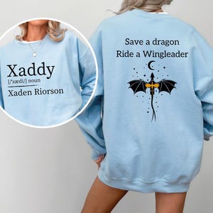 A woman wearing a light blue sweatshirt with a dragon design and text printed on the back.
