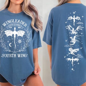 A woman wearing a blue t-shirt with a graphic design featuring a dragon and the text "WINGLEADER - RIDERS QUARANTINE".
