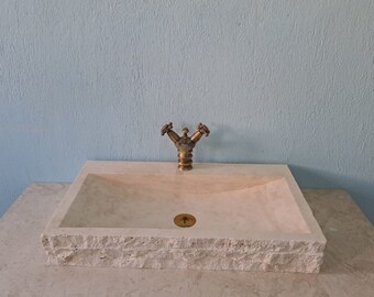 May include: A white stone bathroom sink with a brass faucet. The sink has a rectangular shape with a curved bottom and a textured rim.