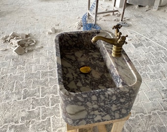 May include: A marble sink with a gold tap. The sink is on a wooden stand and has a purple and white marbled pattern.