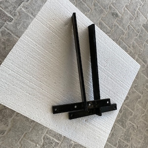 May include: Two black metal brackets with a white background. The brackets are angled and have a flat surface.