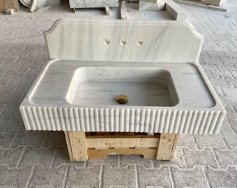 Può includere: Lavabo da bagno in marmo bianco con schienale e bordo scanalato. Il lavabo è montato su una pedana in legno.