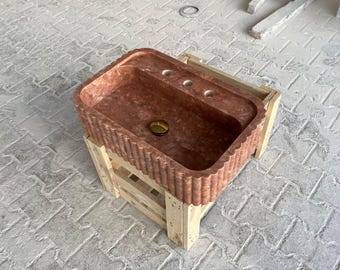 Op de afbeelding: Een rode marmeren gootsteen met een geribbelde rand staat op een houten pallet. De gootsteen heeft drie gaten voor kranen en een afvoer.