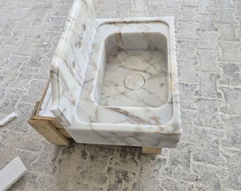 May include: A marble sink with a rectangular basin and a backsplash. The sink features a white and beige veined pattern. The basin has a circular drain. The sink is set on a wooden support.