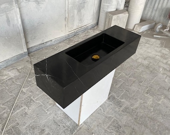 May include: A black marble countertop bathroom sink with a white pedestal base. The sink is rectangular and has a single drain hole. The countertop is polished and has a subtle veining pattern.