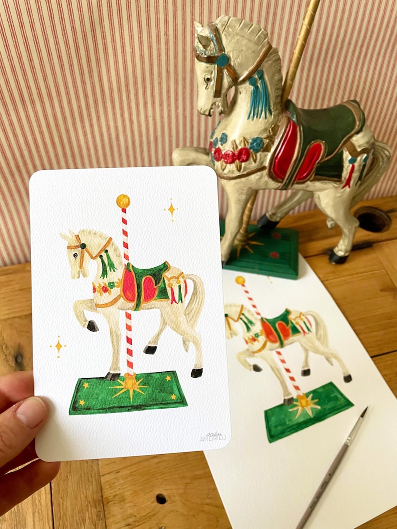 以下が含まれることがあります： メリーゴーランドの馬の置物と、メリーゴーランドの馬の水彩画。 馬は白で、緑と赤のサドルが付いており、赤と白のストライプのポールに取り付けられています。 絵は人の手で持たれています。