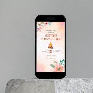 May include: A digital invitation for a Lohri celebration. The invitation features a watercolor background with floral accents and a bonfire illustration. The text reads "Please join us to celebrate Sehaj First Lohri" with the date and time of the event: "January 13 at 06:00 PM". The location is listed as "Party City Hall, 123 Anywhere St., Any City."