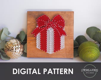 May include: A string art piece depicting a red and white gift box with a bow, mounted on a wooden board. The words "DIGITAL PATTERN" are displayed below the artwork. Decorative gold and green ornaments are on either side.