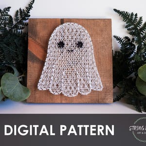 May include: A string art ghost design on a wooden board. The ghost is white with black eyes and a small mouth. The wooden board is brown with a chevron design. The words "DIGITAL PATTERN" are at the bottom of the image.