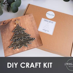 May include: A DIY craft kit with a Christmas tree string art design on a wooden board. The tree is crafted with black string and white dots, and a gold star. The kit comes in a brown cardboard box with a label that reads "String Art Kit Christmas Tree". The text "DIY Craft Kit" is also visible.