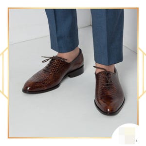 Könnte beinhalten: Braune Lederschuhe mit strukturiertem Muster und Schnürverschluss. Die Schuhe haben eine glänzende Oberfläche und einen niedrigen Absatz. Das Bild zeigt die Schuhe von unten, mit den Beinen des Trägers in blauen Hosen.