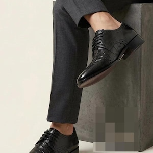 May include: Black leather dress shoes with a textured, crocodile-like pattern. The shoes have a classic lace-up design and a low heel. The image shows the shoes from a low angle, highlighting their polished finish and intricate details.