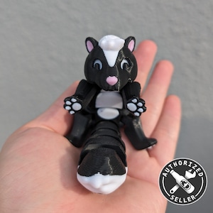 May include: A black and white 3D printed skunk figurine with a white stripe down its back. The skunk is sitting up with its paws outstretched and has a pink nose. The figurine is sitting on a person's hand. The image also includes a black and white sticker with the text "AUTHORIZED SELLER" and a wrench and bottle icon.