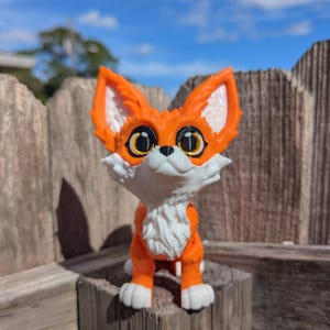 A cute 3D printed fennec fox sits on a fence post. It is orange and white with black and gold eyes. It has huge ears, big eyes, and a clever look on its face.