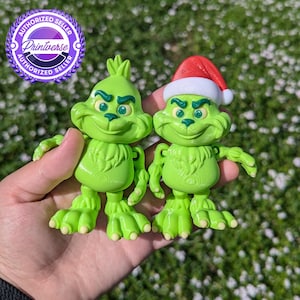May include: Two green Grinch figurines, one wearing a red and white Santa hat. Both have green eyes and a mischievous grin.