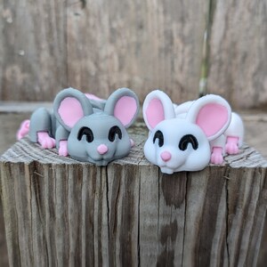 May include: Two small, hand-painted, ceramic mouse figurines. One is gray with pink ears and the other is white with pink ears. Both have black eyes and a pink nose.