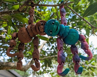 May include: Two colorful articulated toy figures hanging from a tree branch. One figure is brown with a textured surface and the other is blue and purple with a smooth surface.