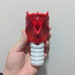 May include: A 3D-printed anatomical model of a larynx, featuring a vibrant red upper section and a white, ribbed lower section. The model is held in a hand, showcasing its detailed structure and design.