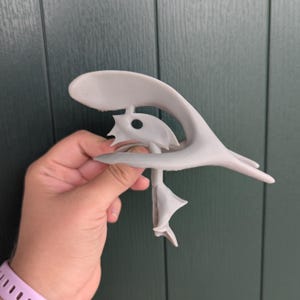 May include: A gray 3D printed sculpture of a stylized bird with a long, curved beak and a hole in the center of its body.