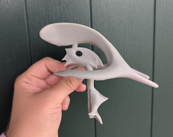 May include: A gray 3D printed sculpture of a stylized bird with a long, curved beak and a hole in the center of its body.