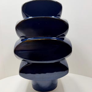 May include: A navy blue ceramic vase with a glossy finish. The vase has a unique stacked design, with rounded, oval-shaped sections. The base is a solid, cylindrical shape. The vase is approximately 12 inches tall.