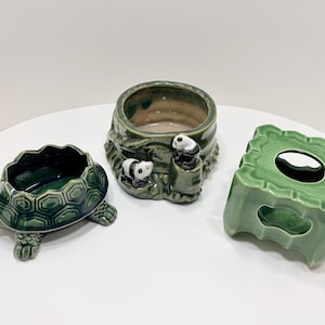 May include: Three ceramic planters in shades of green. One is turtle-shaped, another is a round pot with panda bear figures, and the third is a square-shaped planter with a hole in the center. All are glazed and have a glossy finish.