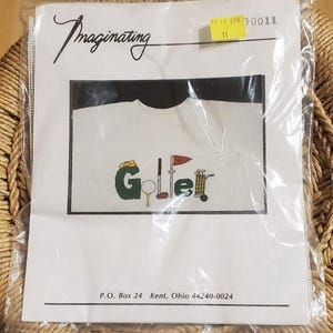 May include: A cross-stitch kit in a plastic package. The package features the word "Imaginating" in cursive. The design shows the word "Golfer" with golf-related images. The text "P.O. Box 24 Kent, Ohio 44240-0024" is printed at the bottom.
