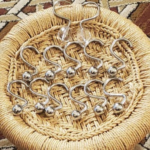 May include: A set of shower curtain hooks with a polished chrome finish. The hooks have a decorative ball at the bottom and a curved S-shape. Two heart-shaped hooks with clear crystal accents are also included.