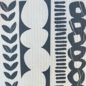 May include: A white rectangular cleaning cloth with a dark gray geometric pattern and the text "ALBERT & HOUSE". The design includes leaf shapes, circles, and lines. Two orange pumpkins are in the background.