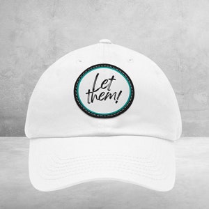 Peut inclure: Casquette de baseball blanche avec un patch circulaire bleu turquoise et noir qui dit "Let them!" en écriture cursive noire.