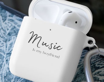 May include: White Airpod case with a black inscription that reads "Music is my boyfriend". The case is open and the Airpods are inside. A silver carabiner clip is attached to the case.