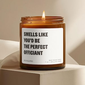May include: A brown glass candle jar with a white label that reads "Smells Like You'd Be The Perfect Officiant". The candle is lit and the label also includes the brand name "HIGHS&JOWS" and the text "Hand Poured Candle 7 oz | 200 g net weight".